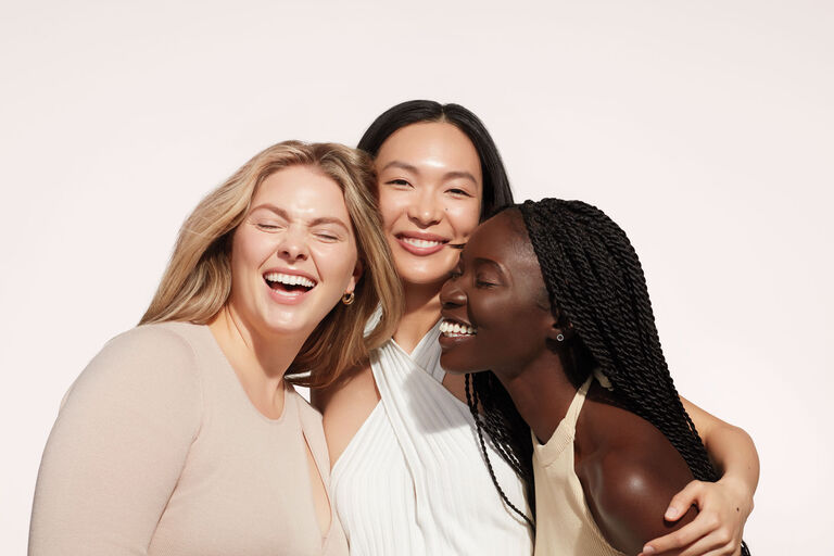 Diverse group of three women with radiant skin hugging and laughing