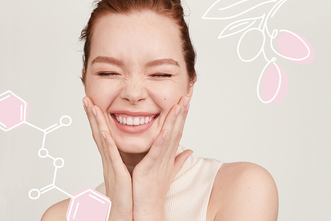 Mujer sonriendo con sus manos en las mejillas, con ilustraciones al fondo de ingredientes activos Mary Kay.