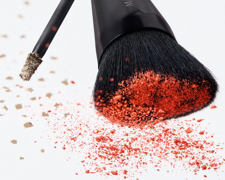 Brow tint applicator and angled cheek brush scattered with loose coral blush