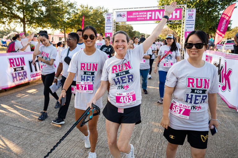 Participants crossing the finish line at a charity 5K race wearing Run for Her shirts