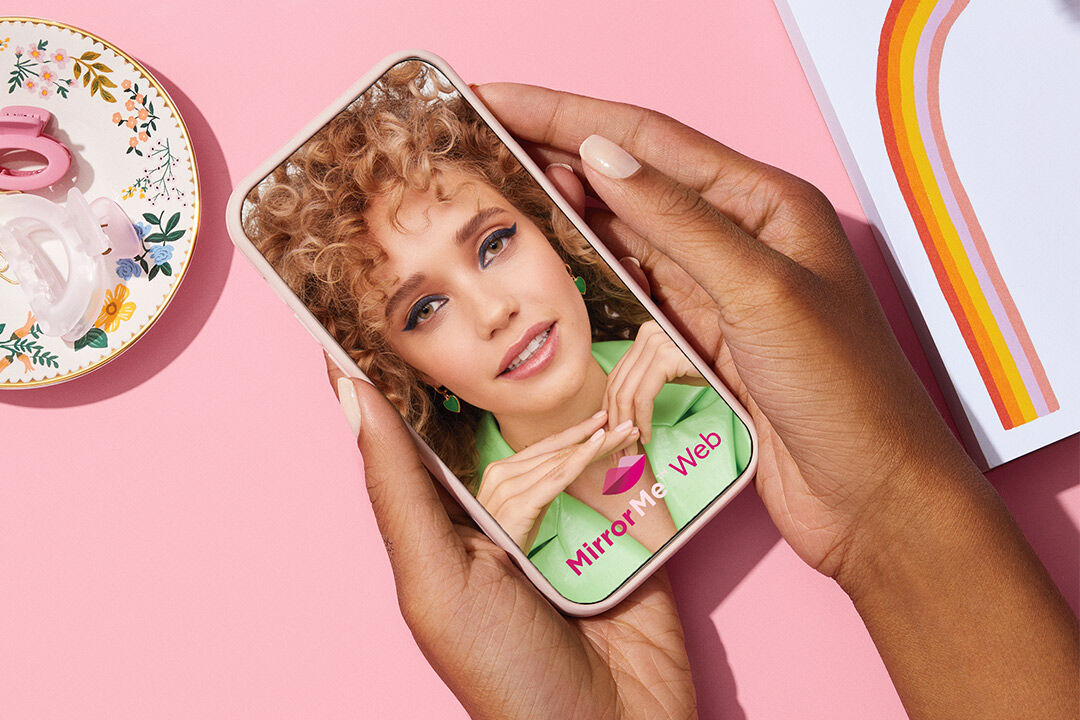 Mano sosteniendo un celular que muestra la experiencia de probador virtual web Mary Kay MirrorMe.