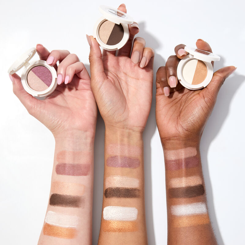 Swatches of special edition Mary Kay At Play Eye Shadow Duo in Rosy Plum, Choco Espresso and Gold Star on light to deep-skinned arms holding compacts image number null