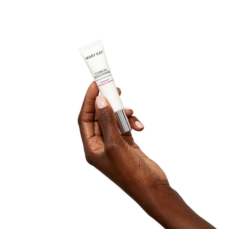 Deep-skinned hand holding tube of Mary Kay Clinical Solutions Dynamic Wrinkle Limiter against a plain background