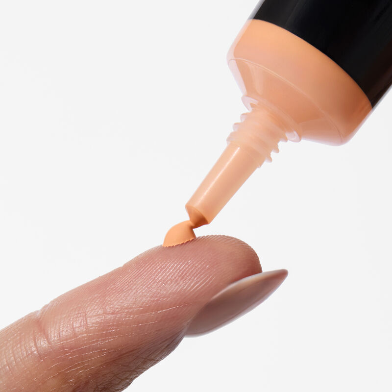 A close-up shot of Mary Kay&reg; Undereye Corrector&rsquo;s needle nose squeezing out a dot of product in shade light peach on a finger&nbsp;
