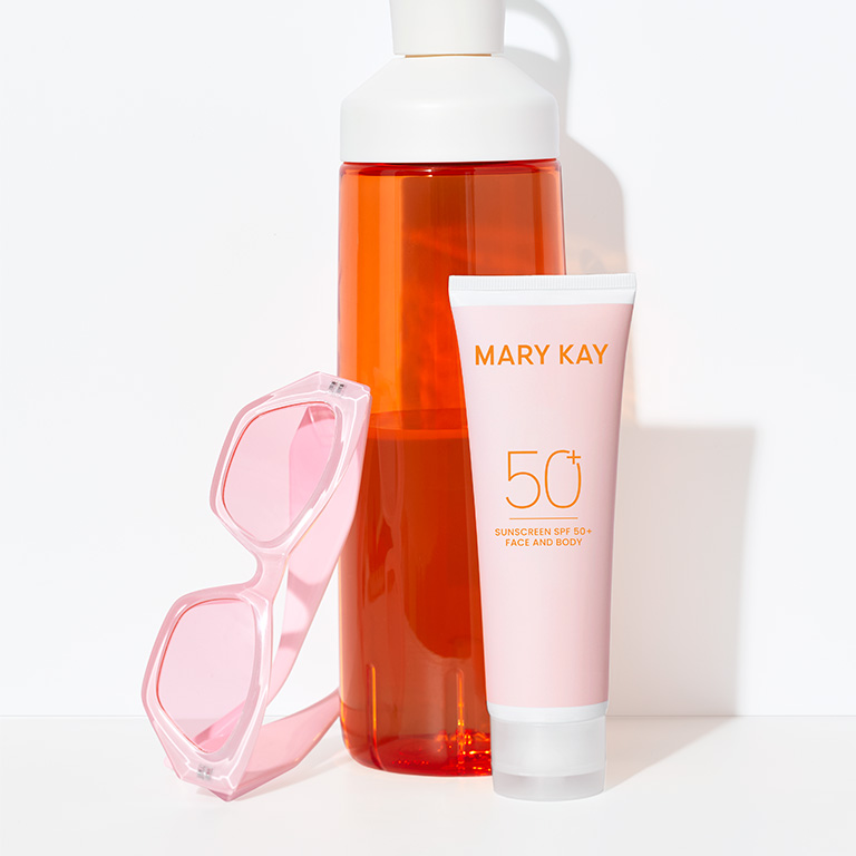 Protector Solar FPS 50+ Mary Kay&reg; junto a una botella de agua naranja y gafas de sol rosas como esenciales de verano.