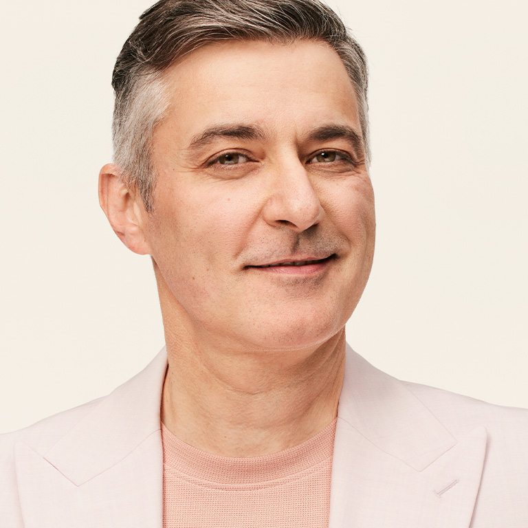 Person having just shaved, wearing a light pink blazer over a neutral top against a plain beige background.